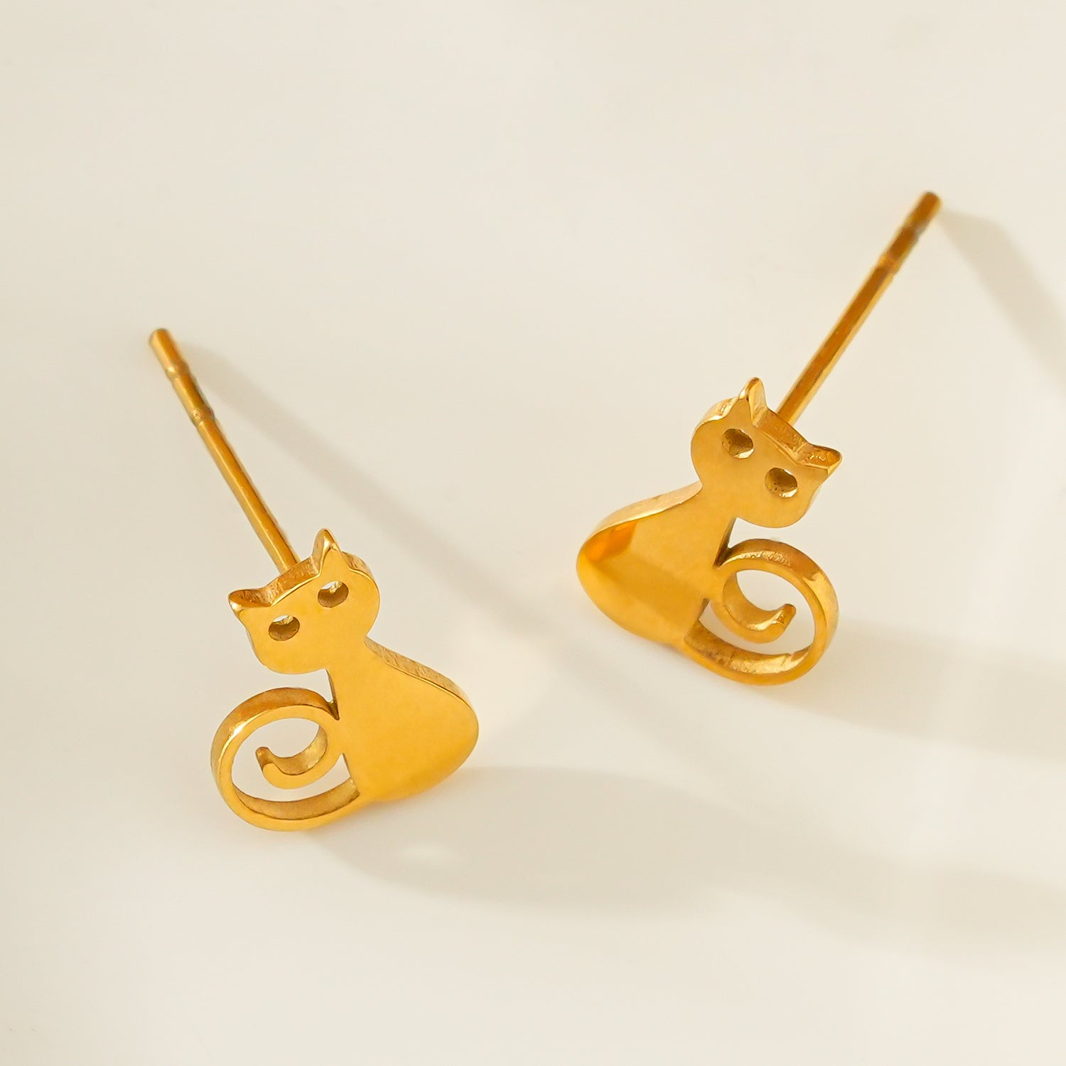 Gold cat-shaped earrings on a light beige background