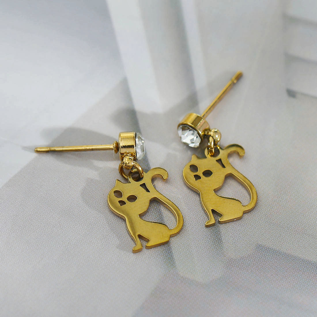 Gold cat-shaped earrings with a clear gemstone on a light gray background