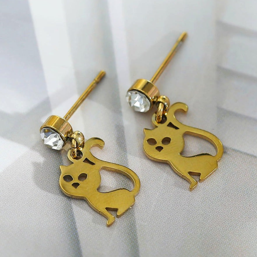 Gold cat-shaped earrings on a white fabric background