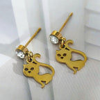Gold cat-shaped earrings on a white fabric background