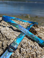 Blue and green patterned strap on a sandy beach with water in the background