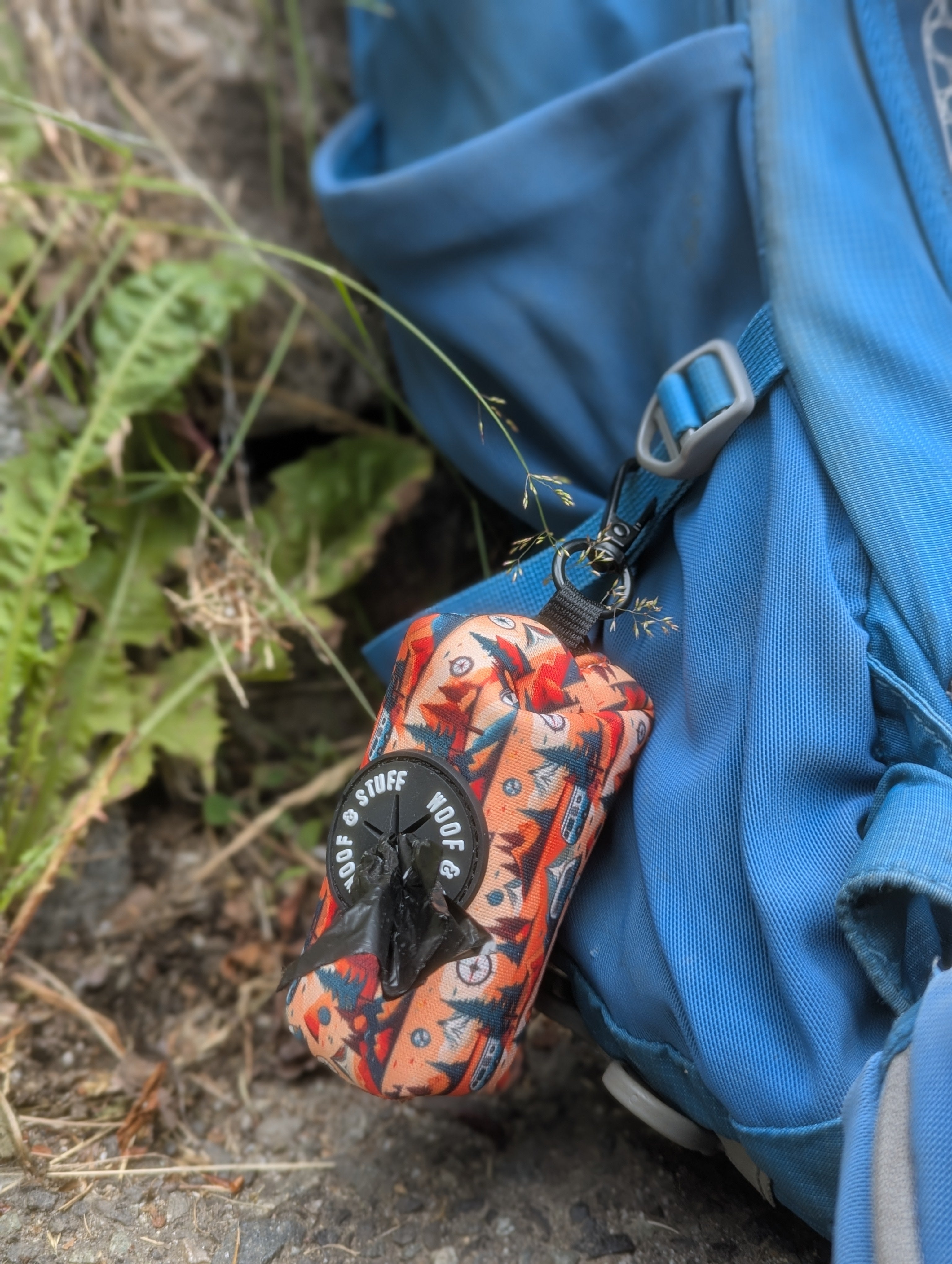 Orange and black dog waste bag attached to a blue backpack on a natural background