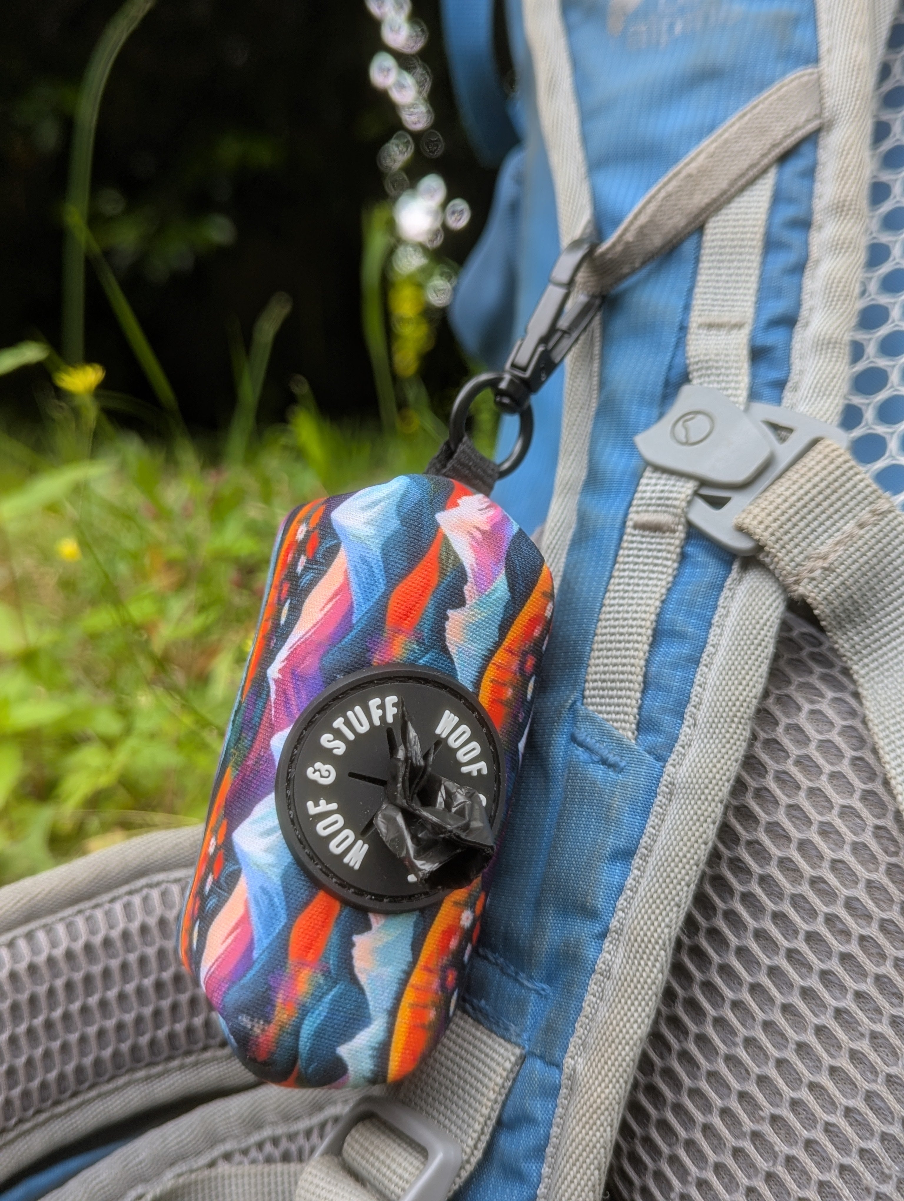 Colorful poop bag dispenser attached to a backpack with a natural background