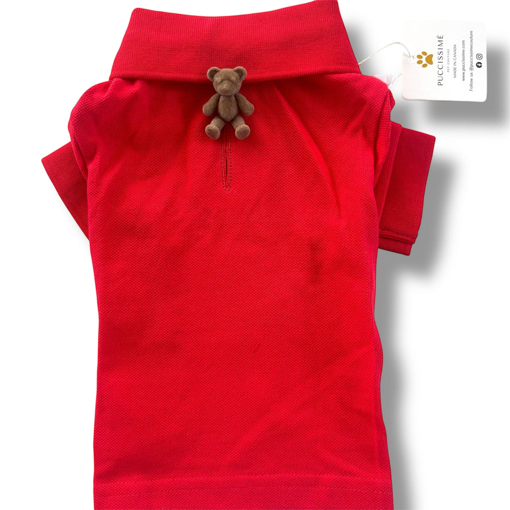 Red dog polo shirt with a small teddy bear attached to the collar on a white background.