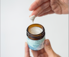 Hand holding a small jar of natural dog toothpaste with a person applying a white paste to a finger.