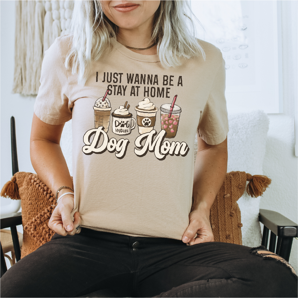 Person wearing a beige t-shirt with 'I Just Wanna Be a Stay at Home Dog Mom' text and graphics.