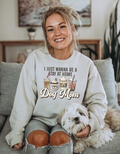 Woman wearing a sweatshirt with 'I just wanna be a stay at home dog mom' text, sitting on a couch with a dog.