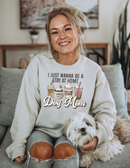 Woman wearing a sweatshirt with 'I just wanna be a stay at home dog mom' text, sitting on a couch with a dog.