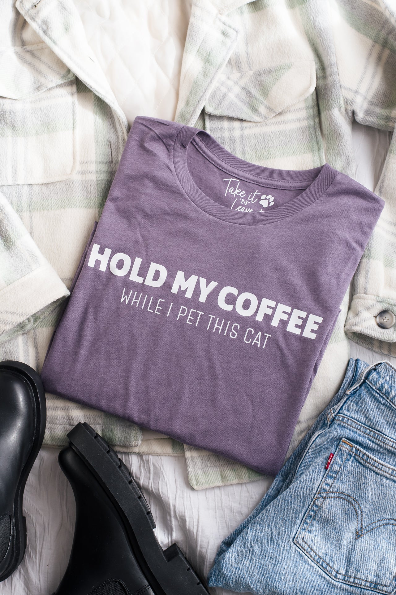 Purple t-shirt with text 'Hold my coffee while I pet this cat' on a checkered fabric background.