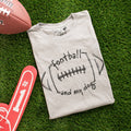 Folded t-shirt with 'football and my dog' text on grass with football and foam finger