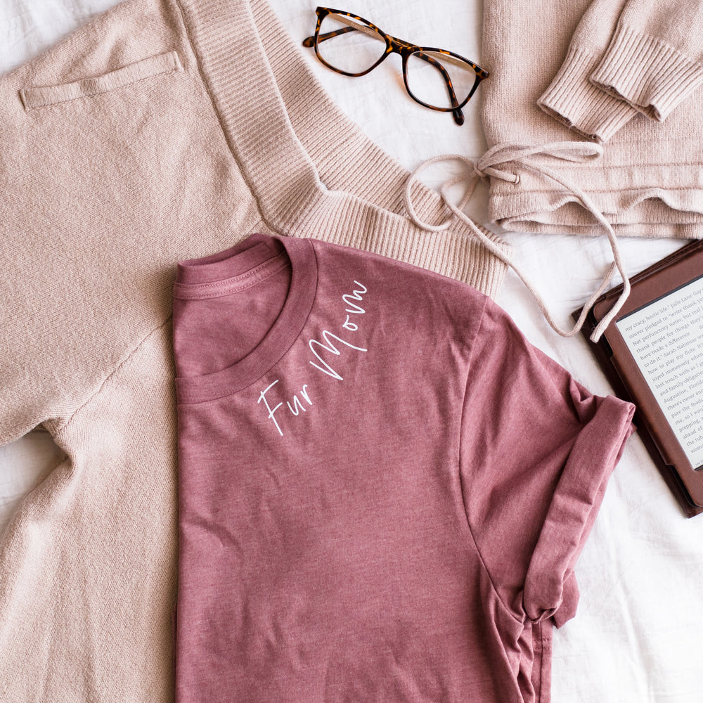 Pink t-shirt with 'Far Mom' text on a light surface with beige pants and glasses.