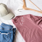 Pink t-shirt with 'For Mom' text, blue jeans, and a cap on a white surface.