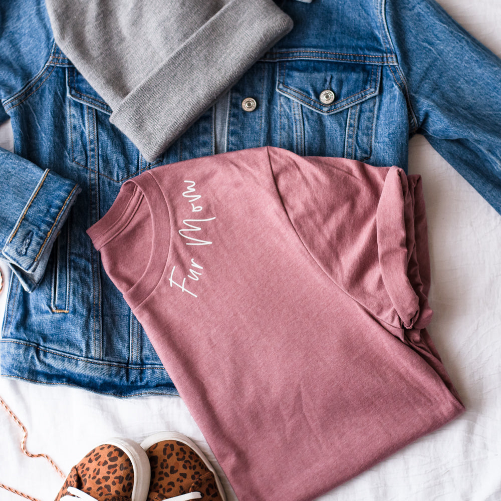 Pink sweatshirt with text, blue denim jacket, gray beanie, and leopard print sandals on a white surface