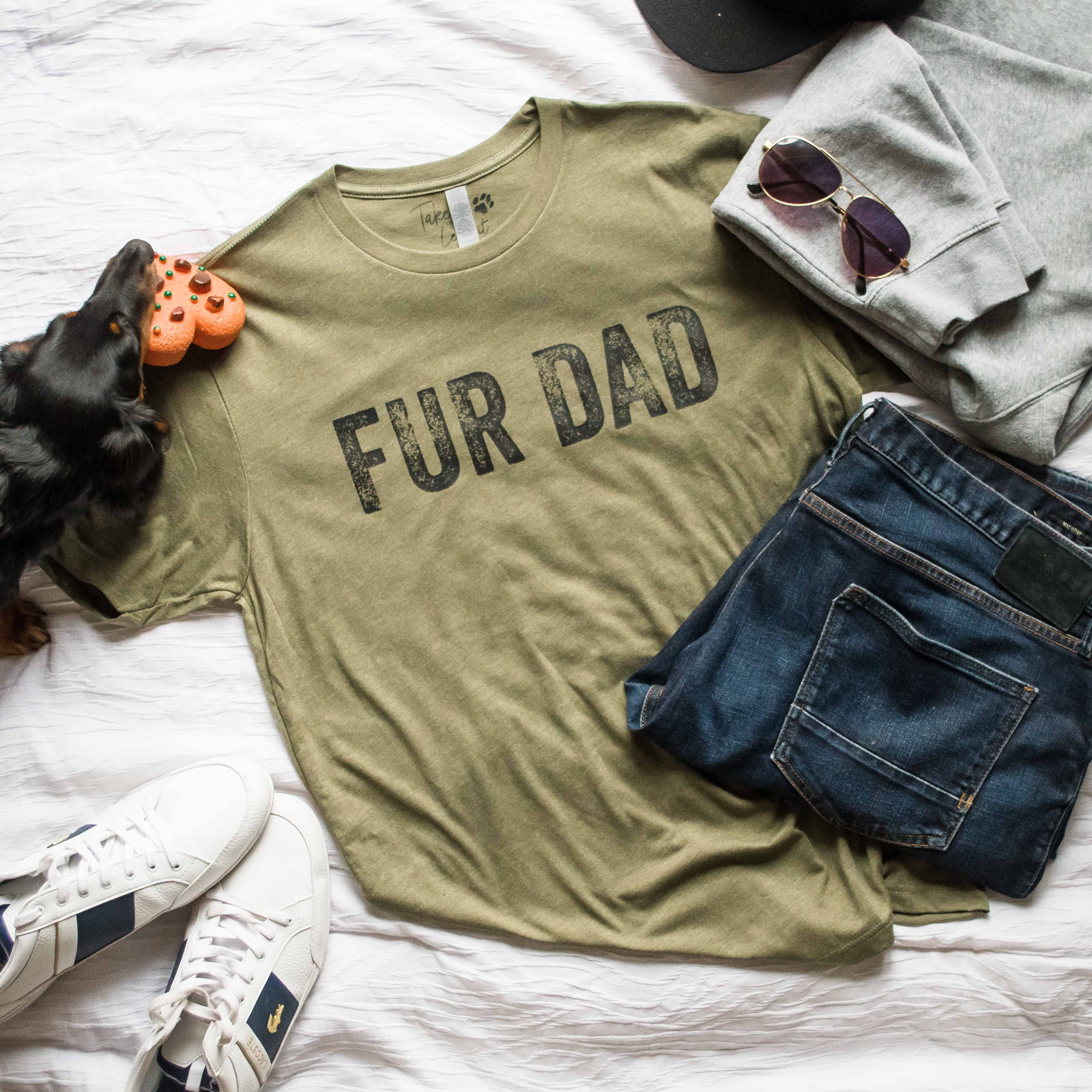 Green t-shirt with 'FUR DAD' text on a bed with jeans, sneakers, and a dog toy.