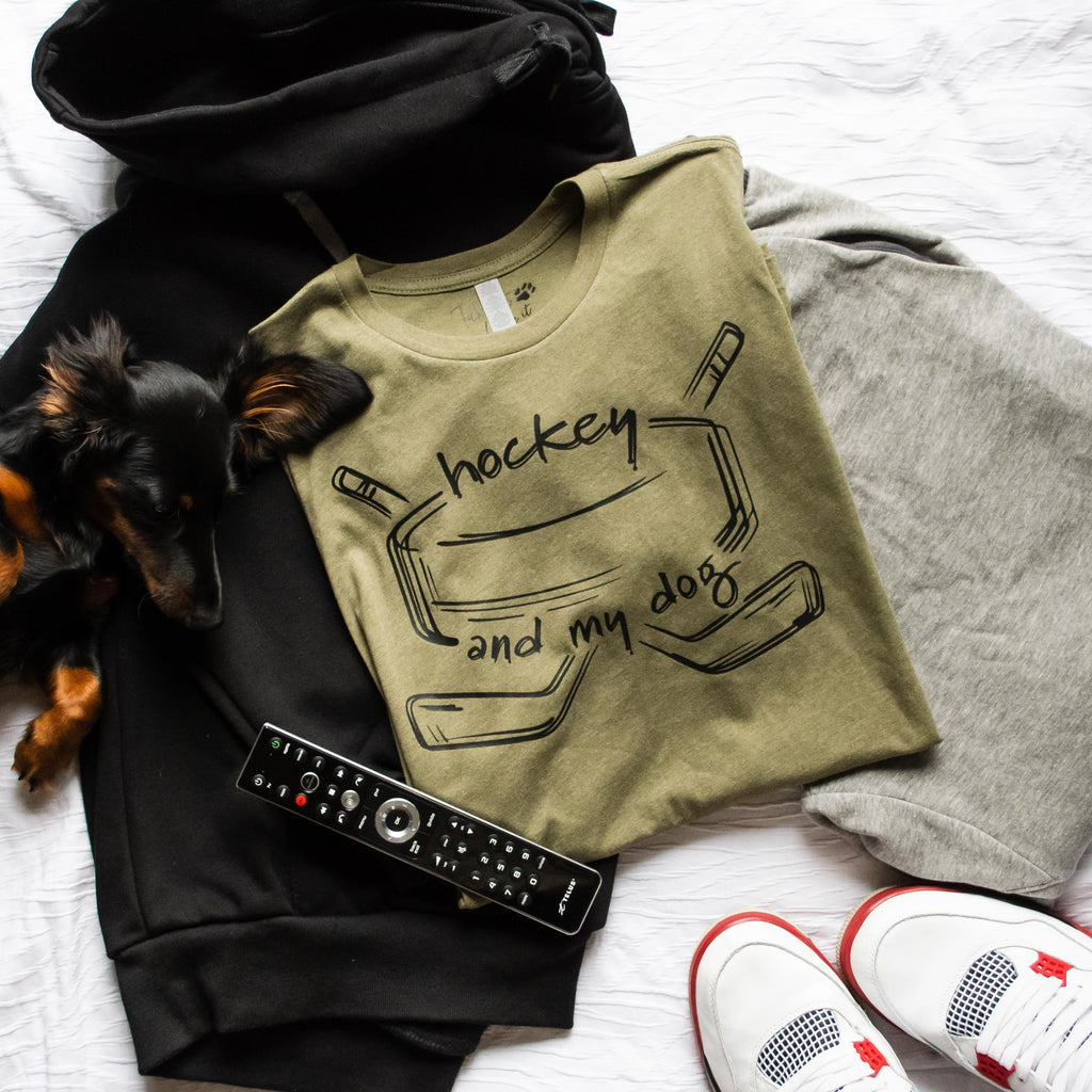 Folded sweatshirt with 'hockey and my dog' design, remote control, and shoes on a white surface.