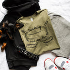 Folded sweatshirt with 'hockey and my dog' design, remote control, and shoes on a white surface.