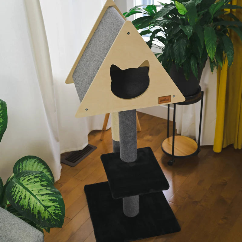 Cat tree with a black cat face design on a wooden floor with plants around