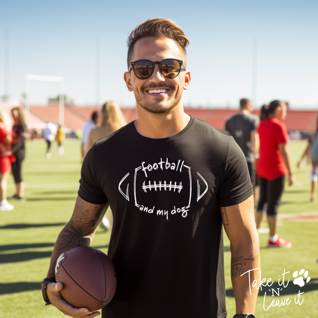 Man holding a football on a sports field wearing a black t-shirt with text.