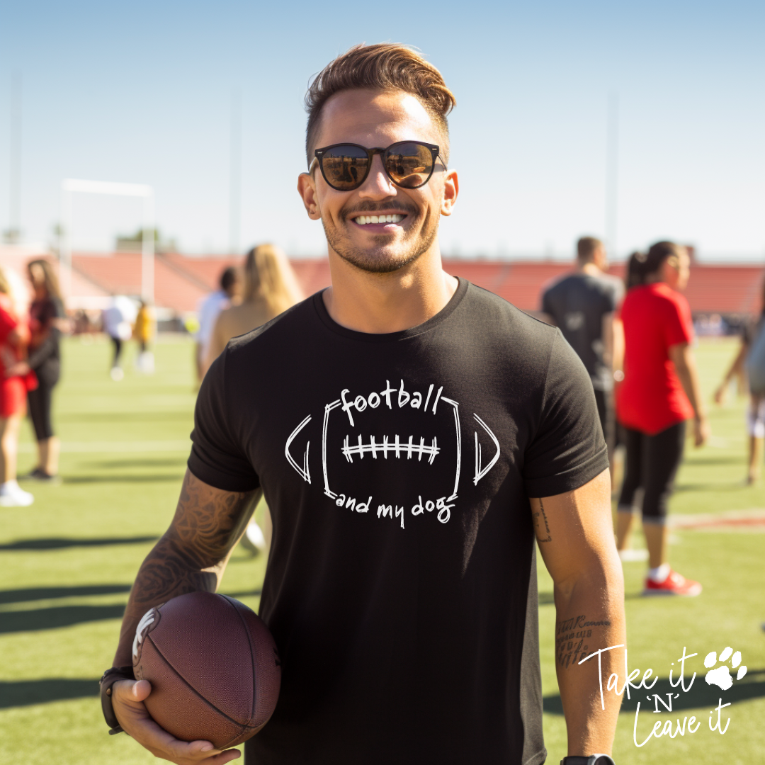 Man holding a football on a sports field wearing a black t-shirt with text.