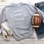 Gray sweatshirt with 'football and my dog' text, Wilson NCAA football, jeans, and white sneakers on a wooden surface.