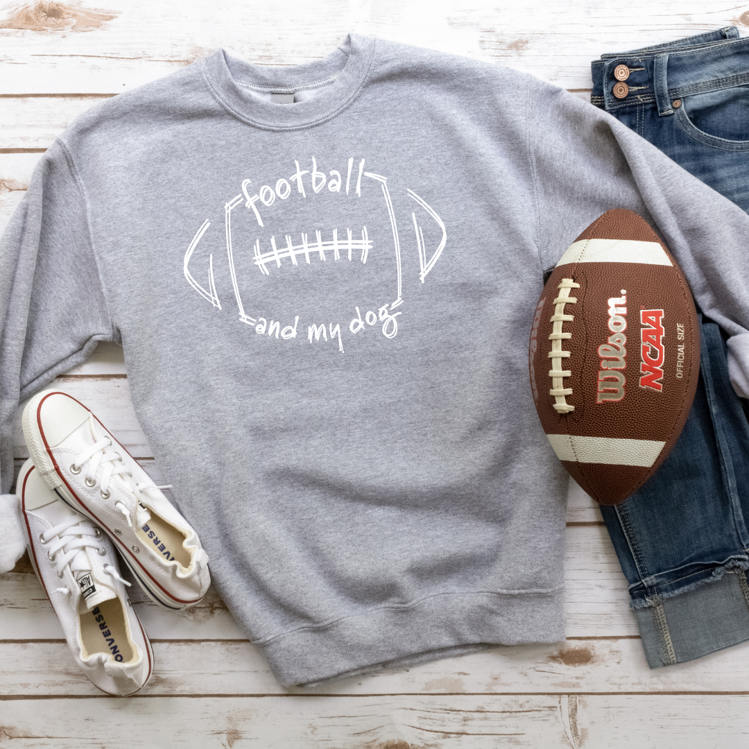 Gray sweatshirt with 'football and my dog' text, Wilson NCAA football, jeans, and white sneakers on a wooden surface.