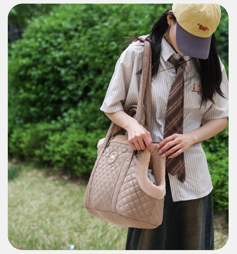 Person holding a quilted pet carrier outdoors with greenery in the background