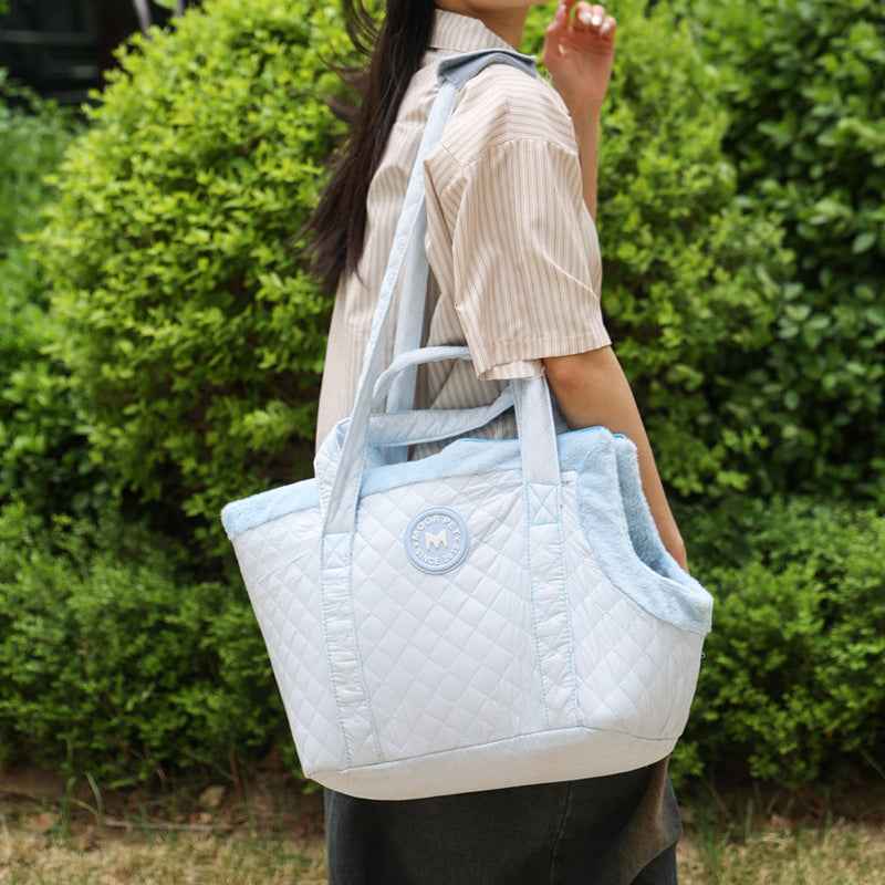 Person holding a light blue quilted pet carrier with a green outdoor background