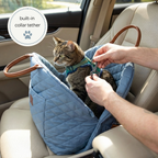 Cat in a blue car seat with a person adjusting a collar tether, inside a vehicle.