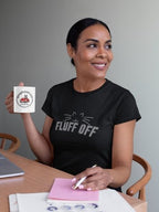 Woman holding a mug with a logo and text, wearing a black t-shirt with 'FLUFF OFF' print.