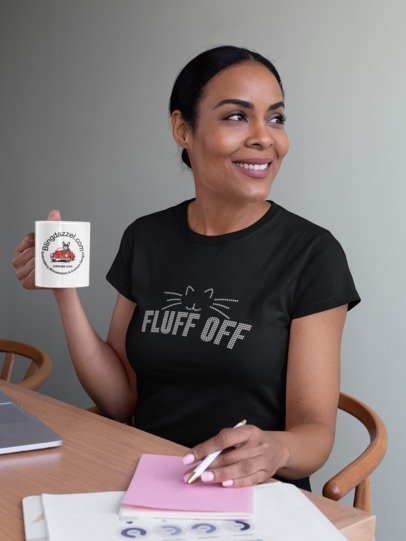 Woman holding a mug with a logo and text, wearing a black t-shirt with 'FLUFF OFF' print.
