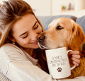 Woman holding a mug with a dog, both sitting on a couch.