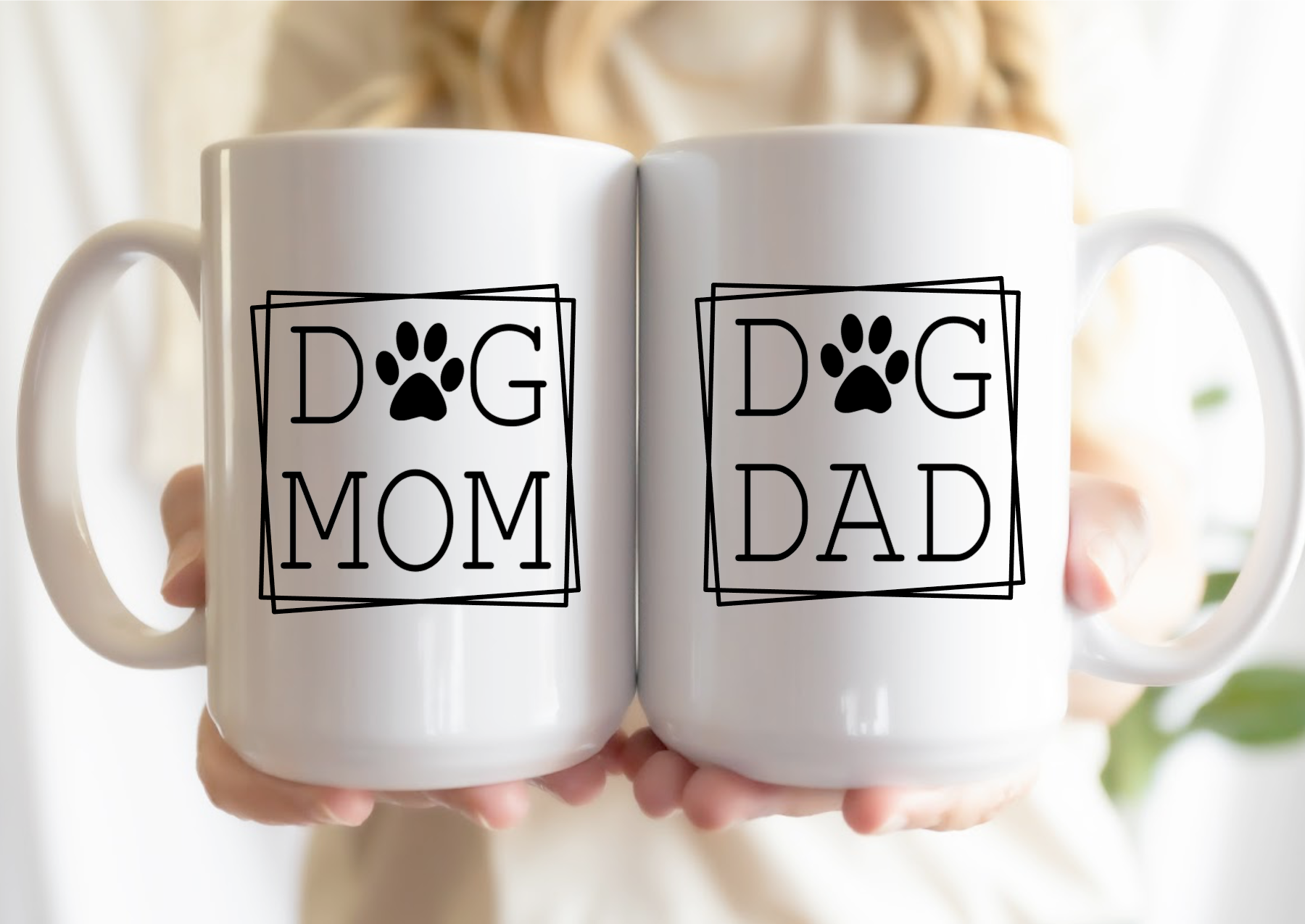 Two white mugs with 'Dog Mom' and 'Dog Dad' text held together.
