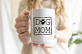 Person holding a white mug with 'DOG MOM' text and paw print design.