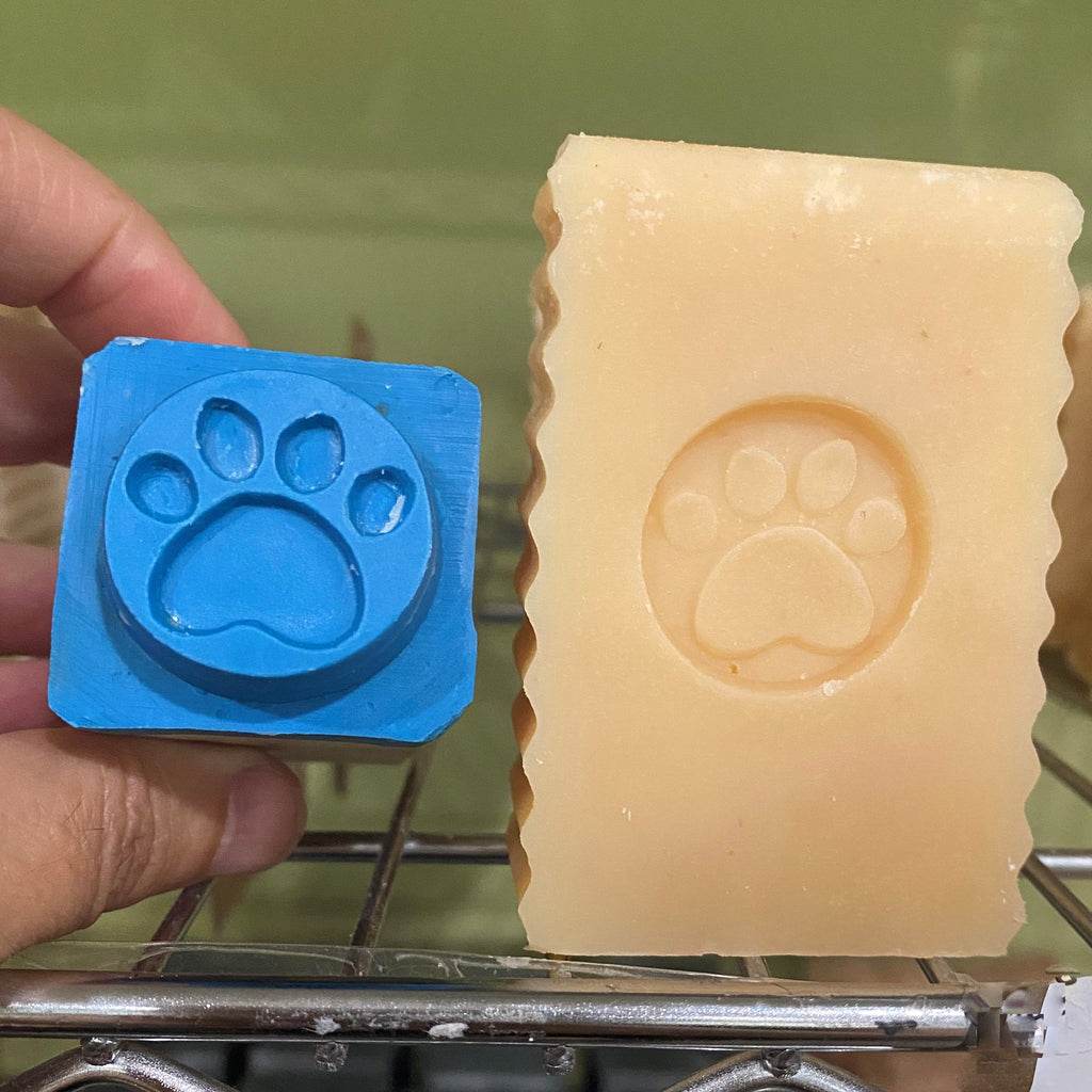 Bar of soap with a paw print impression next to a blue mold with a paw print on a metal rack.