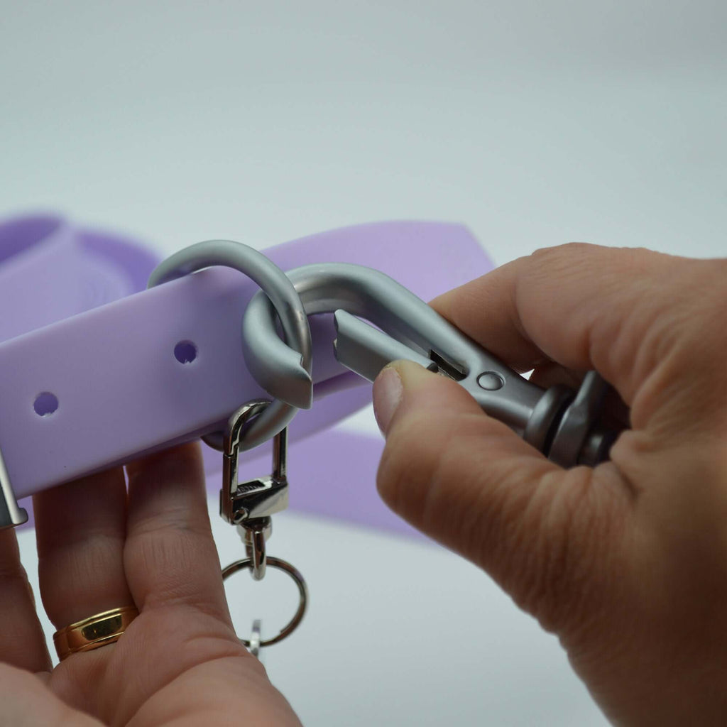Person attaching a carabiner to a purple object with a plain background
