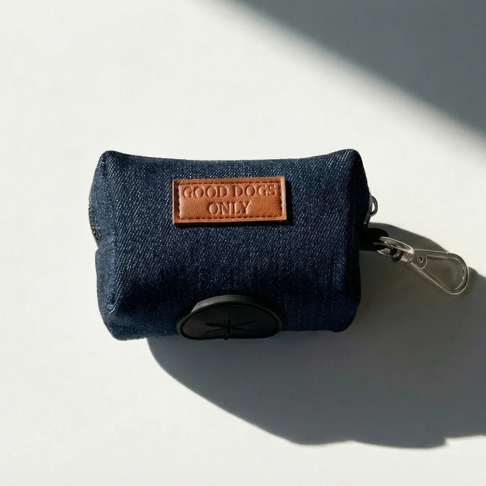 Blue denim dog waste bag holder with a brown leather patch labeled 'Good Dogs Only' on a light background