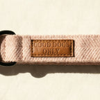 Pink dog collar with a brown leather patch labeled 'Good Dogs Only' on a beige background