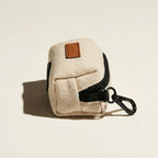 Beige fabric dog waste bag dispenser with black zipper and brown leather tag on a beige background