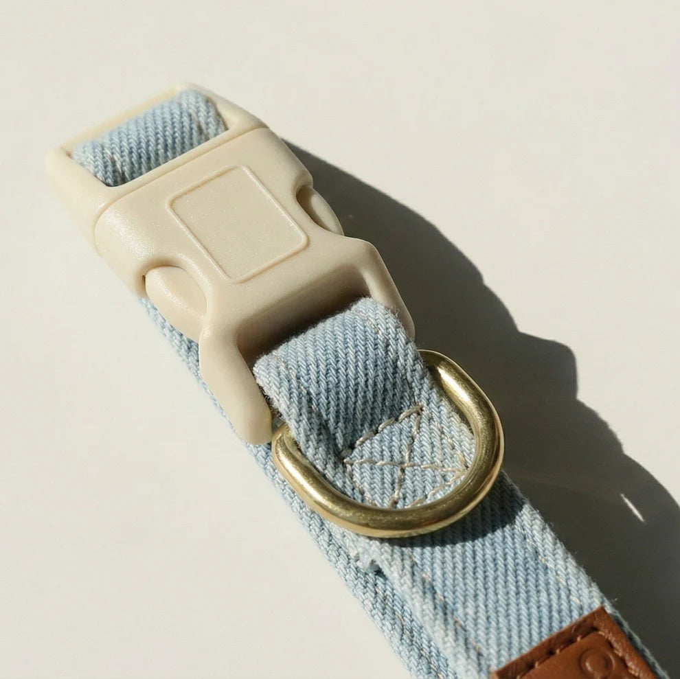 Denim strap with beige buckle and brass ring on a light background
