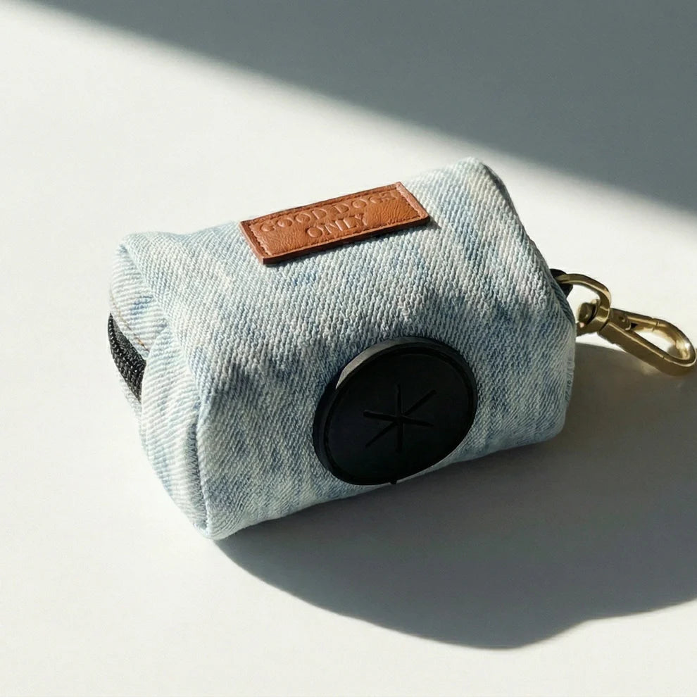 Denim dog waste bag holder and gold keychain on a light gray background