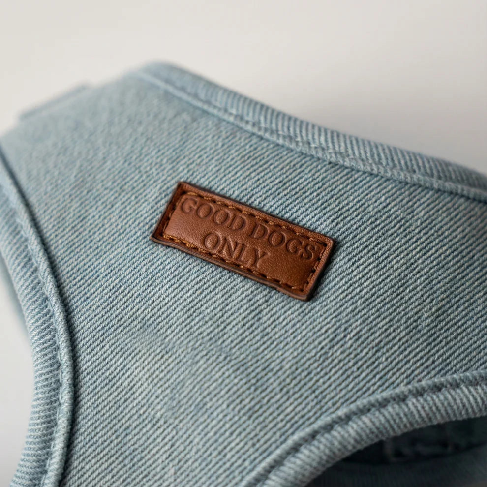 Light blue denim dog harness with a brown leather label reading 'Good Dogs Only' on a light gray background.