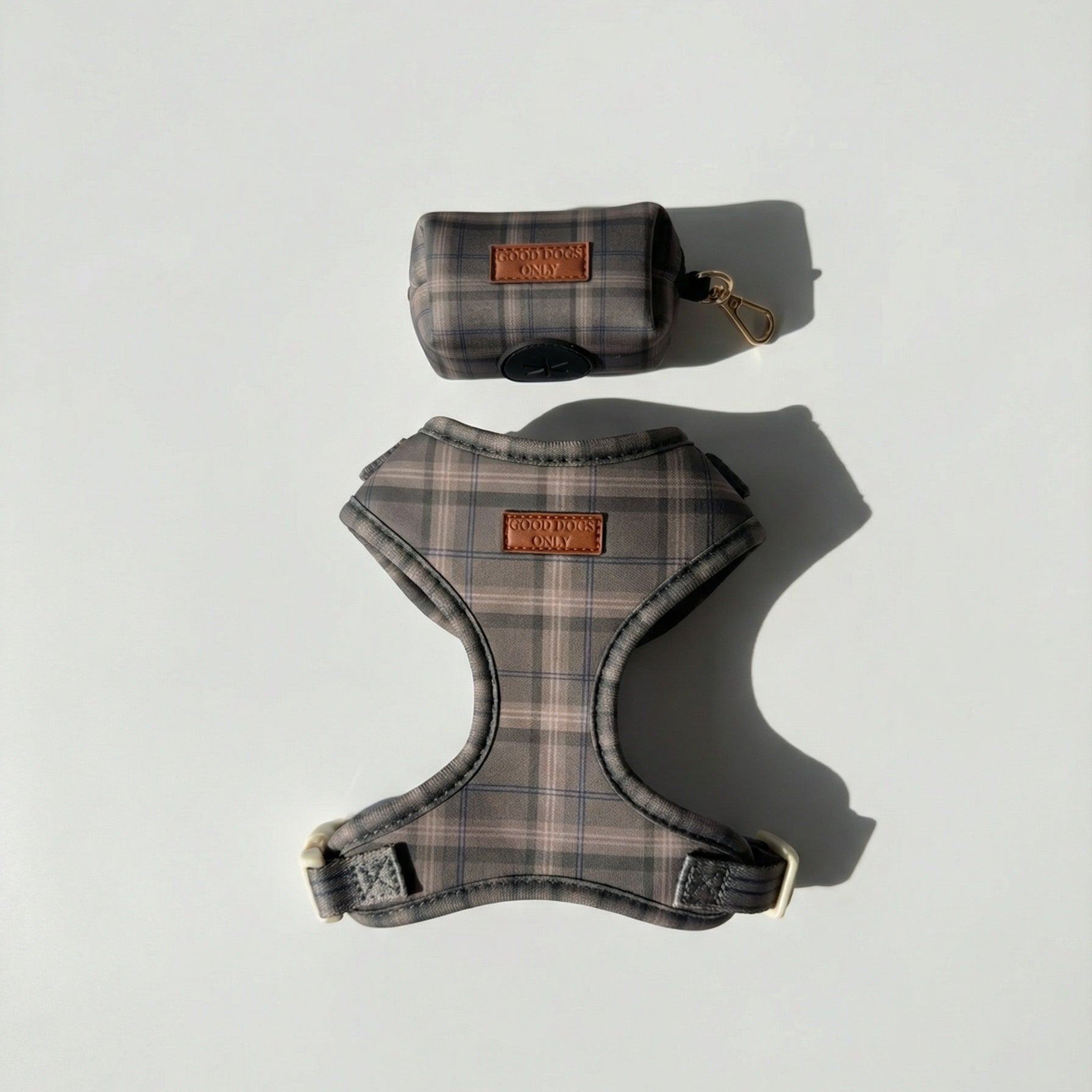 Plaid dog harness and a dog waste bag pouch on a light gray background
