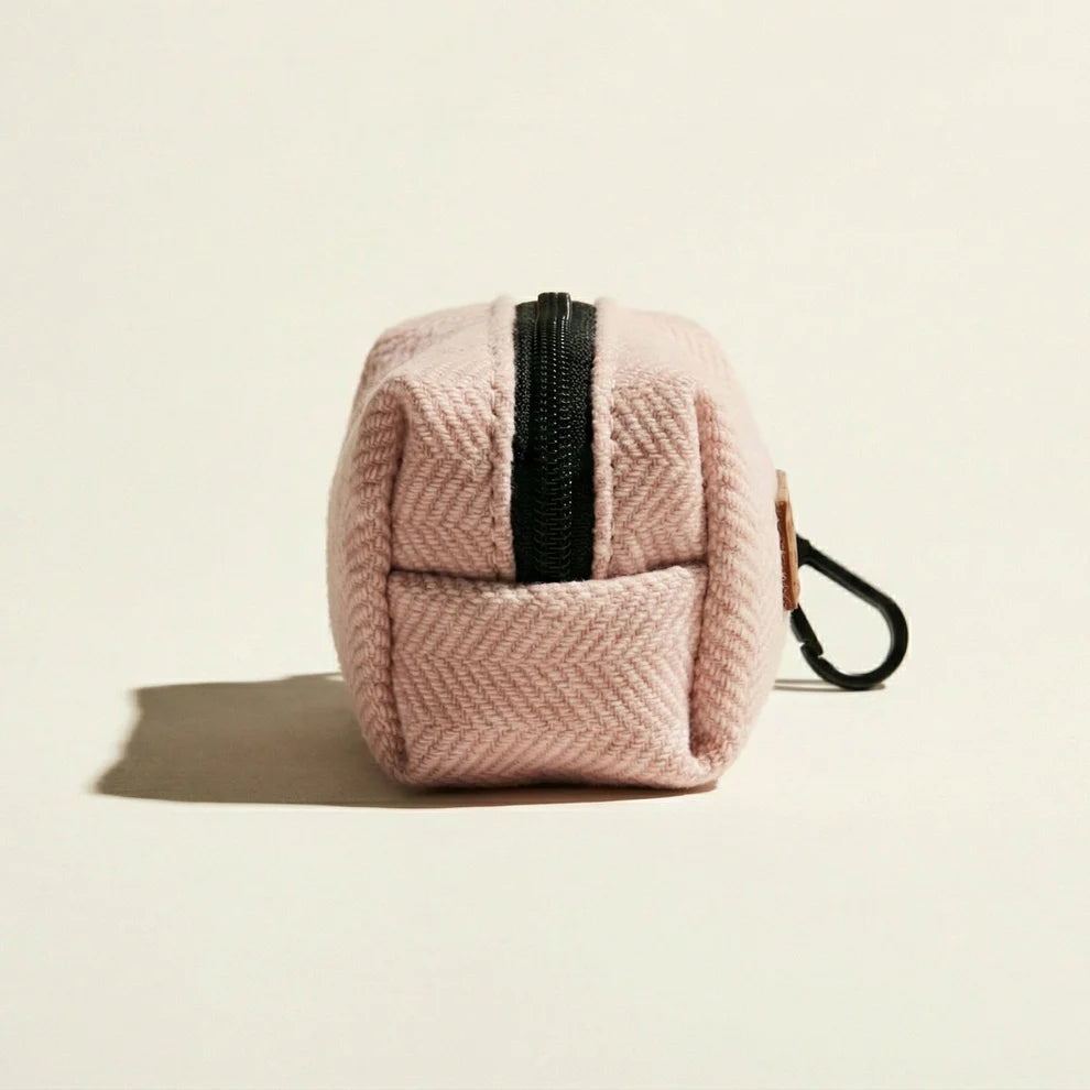 Pink textured dog waste bag holder with a black zipper on a beige background