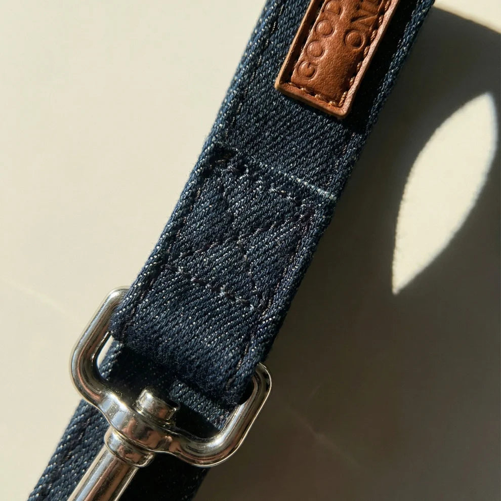 Close-up of a denim leash with a metal buckle and brown leather patch on a beige background