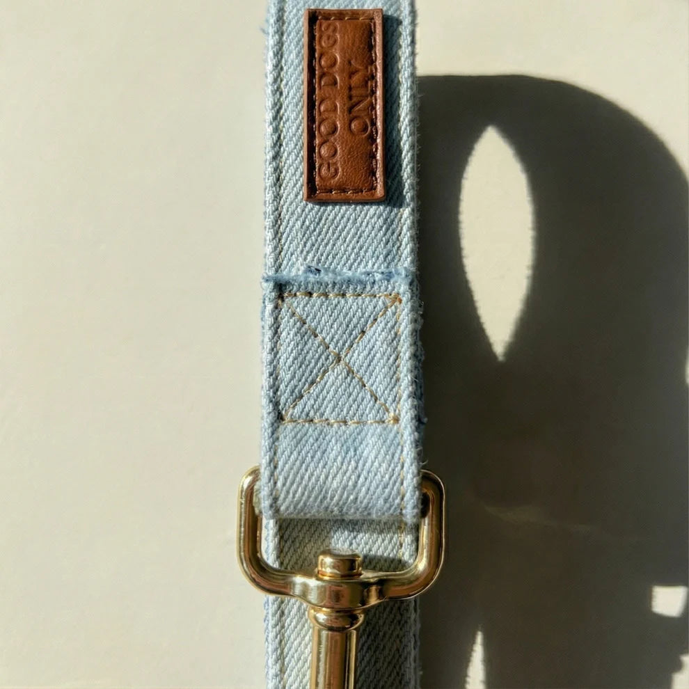 Denim dog leash with gold hardware and leather tag on a neutral background