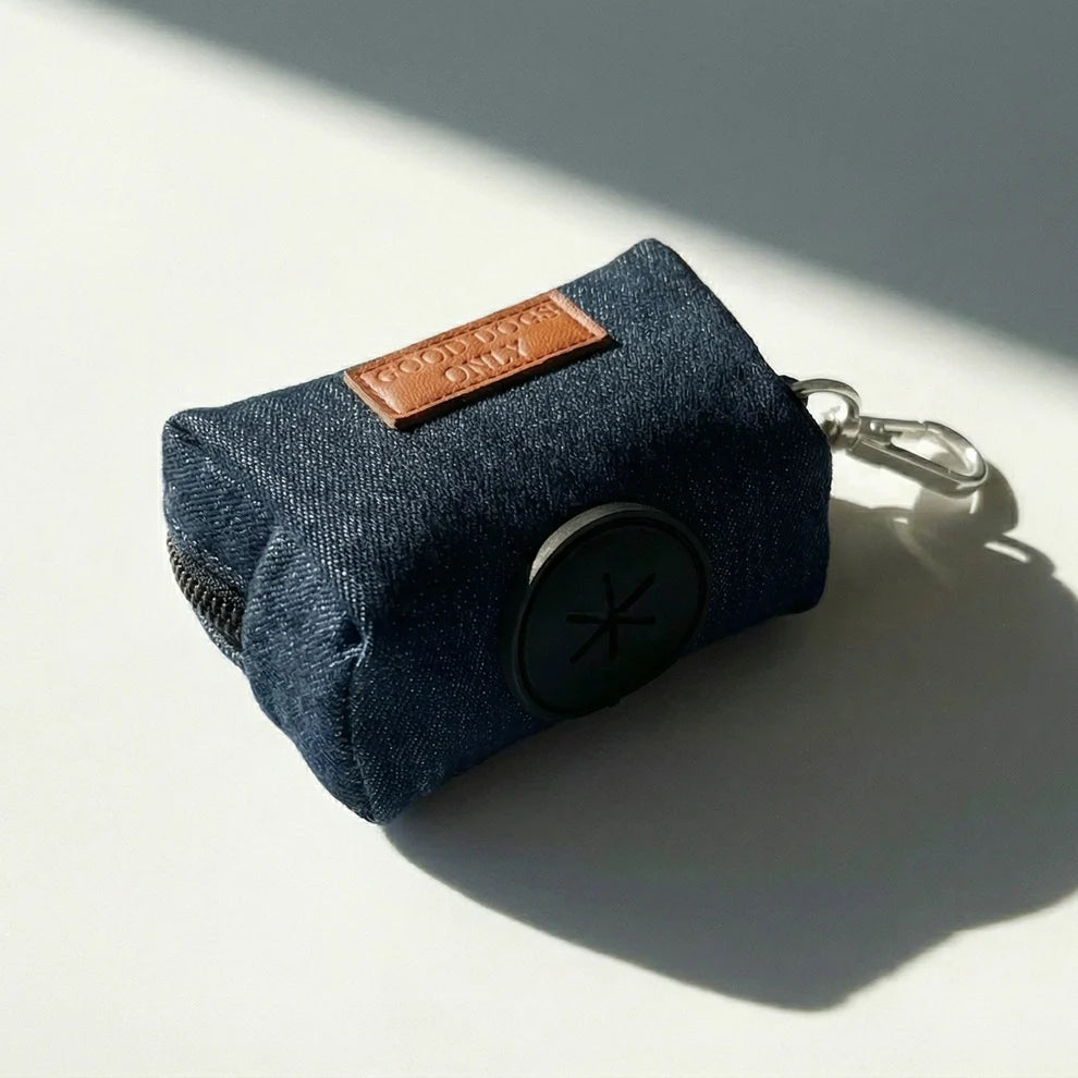 Blue denim dog waste bag holder with a brown leather patch and keychain on a light background