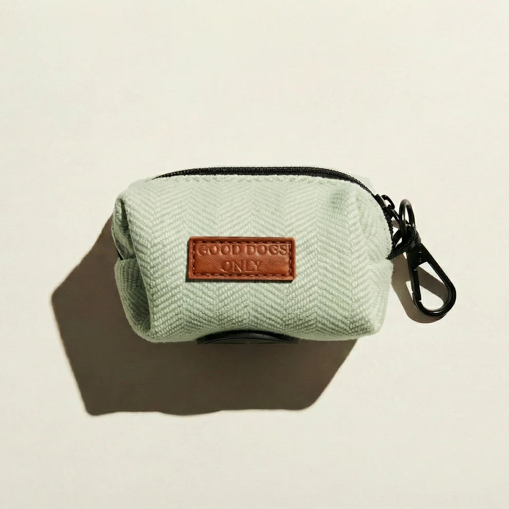 Light green dog waste bag holder with a brown leather patch labeled 'Good Dogs Only' on a beige background