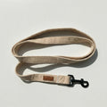 Beige dog leash with a brown leather patch on a light gray background