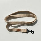 Beige dog leash with a brown leather patch on a light gray background