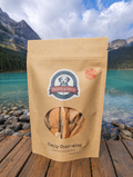 Kraft paper bag with a brand label on a wooden platform by a scenic lake with mountains.